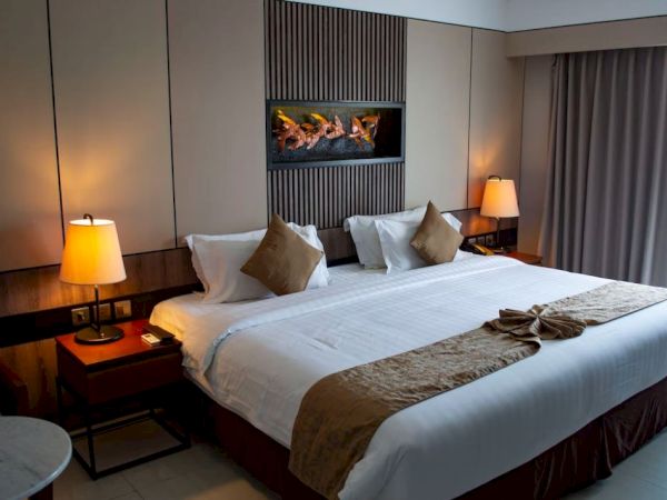 A well-decorated hotel room featuring a large bed with two pillows, bedside tables with lamps, and a contemporary wall-mounted artwork.