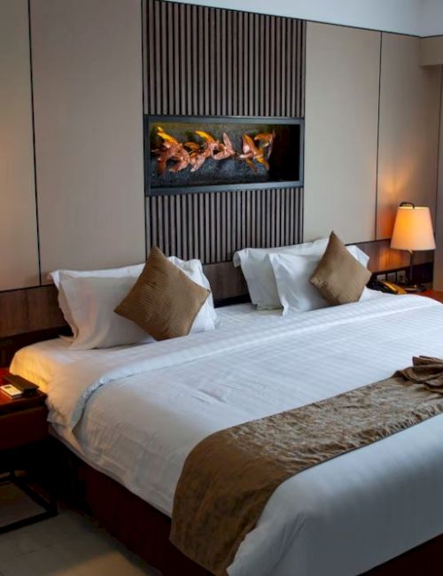 A neatly made hotel room features a large bed, two bedside lamps, neutral tones, and a decorative wall piece above the headboard.