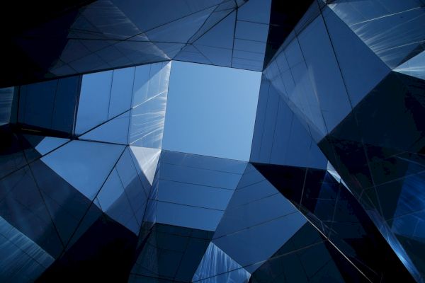 The image shows a geometrical arrangement of reflective glass structures, forming a skylight that opens up to a blue sky.