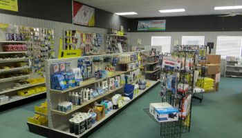 This is an image of a hardware or supply store with shelves filled with various items such as paint, cleaning supplies, and tools.