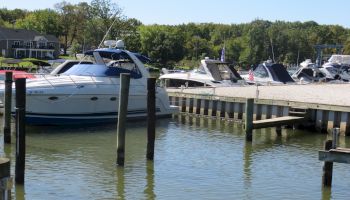 The image shows a marina with several boats docked, including a large yacht in the foreground and more boats in the background.