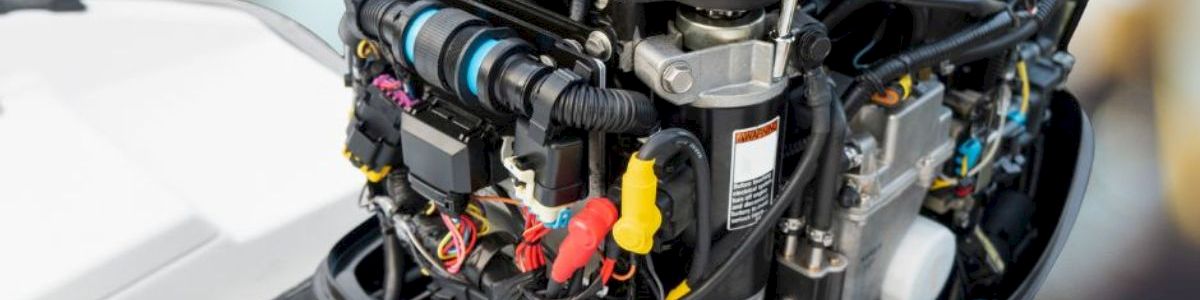 Outboard motor with exposed engine wiring and components, a technician&rsquo;s gloved hand adjusting a tool on top.