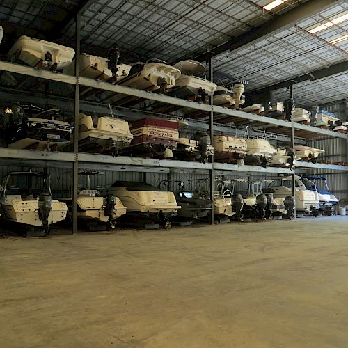 The image shows a storage facility with multiple boats stacked on three levels of shelves in a spacious warehouse.