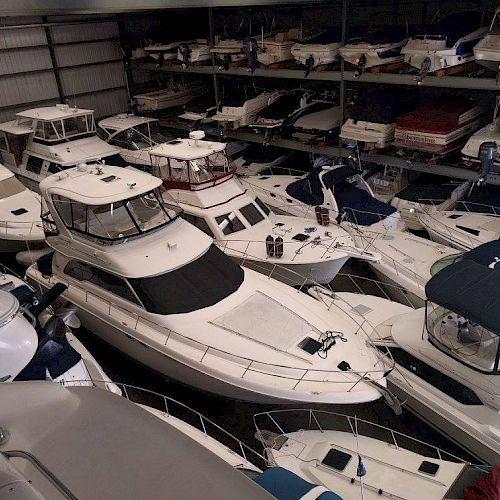 The image shows an indoor storage facility filled with various boats and yachts, arranged closely together in multiple rows.