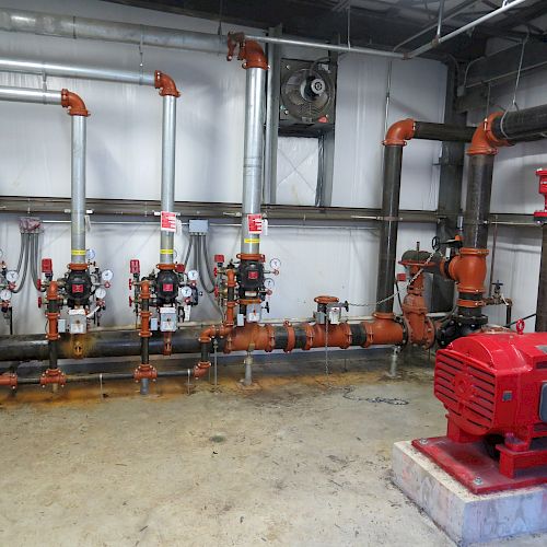 The image shows an industrial setup with multiple pipes, valves, and a large red pump, likely part of a mechanical or plumbing system for liquid distribution.