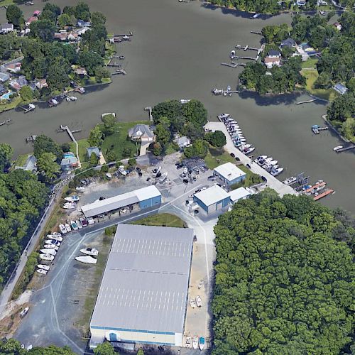 Aerial view of a waterfront area with docks, boats, buildings, roads, and surrounding wooded and residential areas.