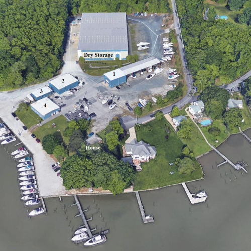 The image shows an aerial view of a marina with boats docked, a park, dry storage, buildings, and surrounding greenery along a waterfront.