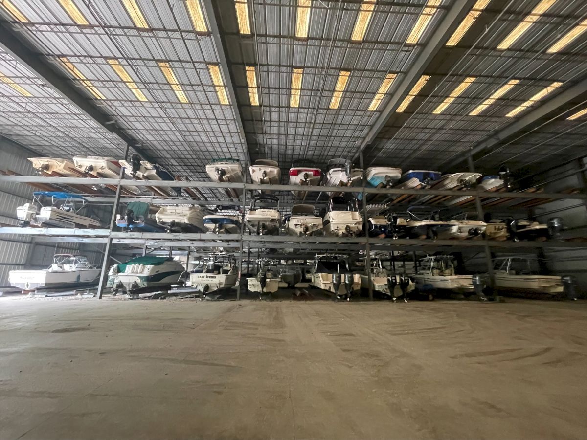 A multi-level car storage yard with numerous vehicles stacked on metal shelves inside a warehouse, awaiting pickup or repair.