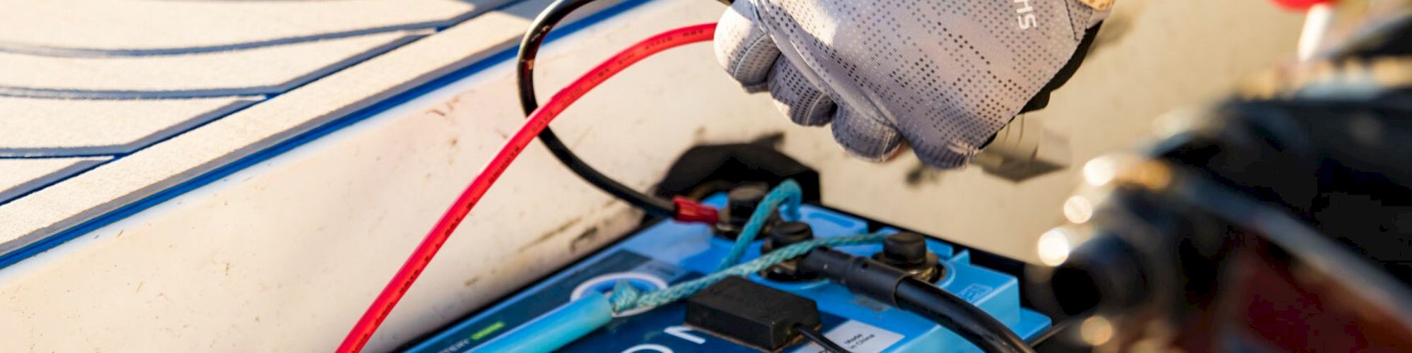 A mechanic's setup with a car battery being tested, red/black cables, and a gloved hand nearby, amid blue tools and equipment, to keep power flowing.