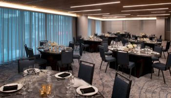 An elegantly set dining area with round tables, black chairs, and ambient lighting, ready for an event with table settings of plates and glasses.