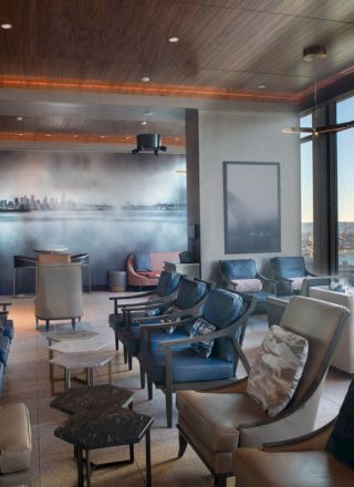 A modern lounge area with comfortable seating, large windows offering a scenic view of a cityscape and water, and a minimalist interior design.