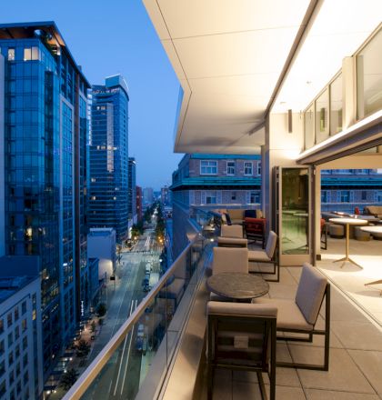 The image shows a modern cityscape viewed from a high-rise building's balcony at dusk, featuring a mix of residential and commercial buildings.