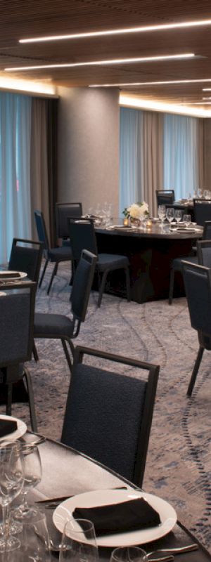 The image shows an elegantly set banquet hall with multiple round tables, each set with black napkins, glassware, and floral centerpieces under soft lighting.