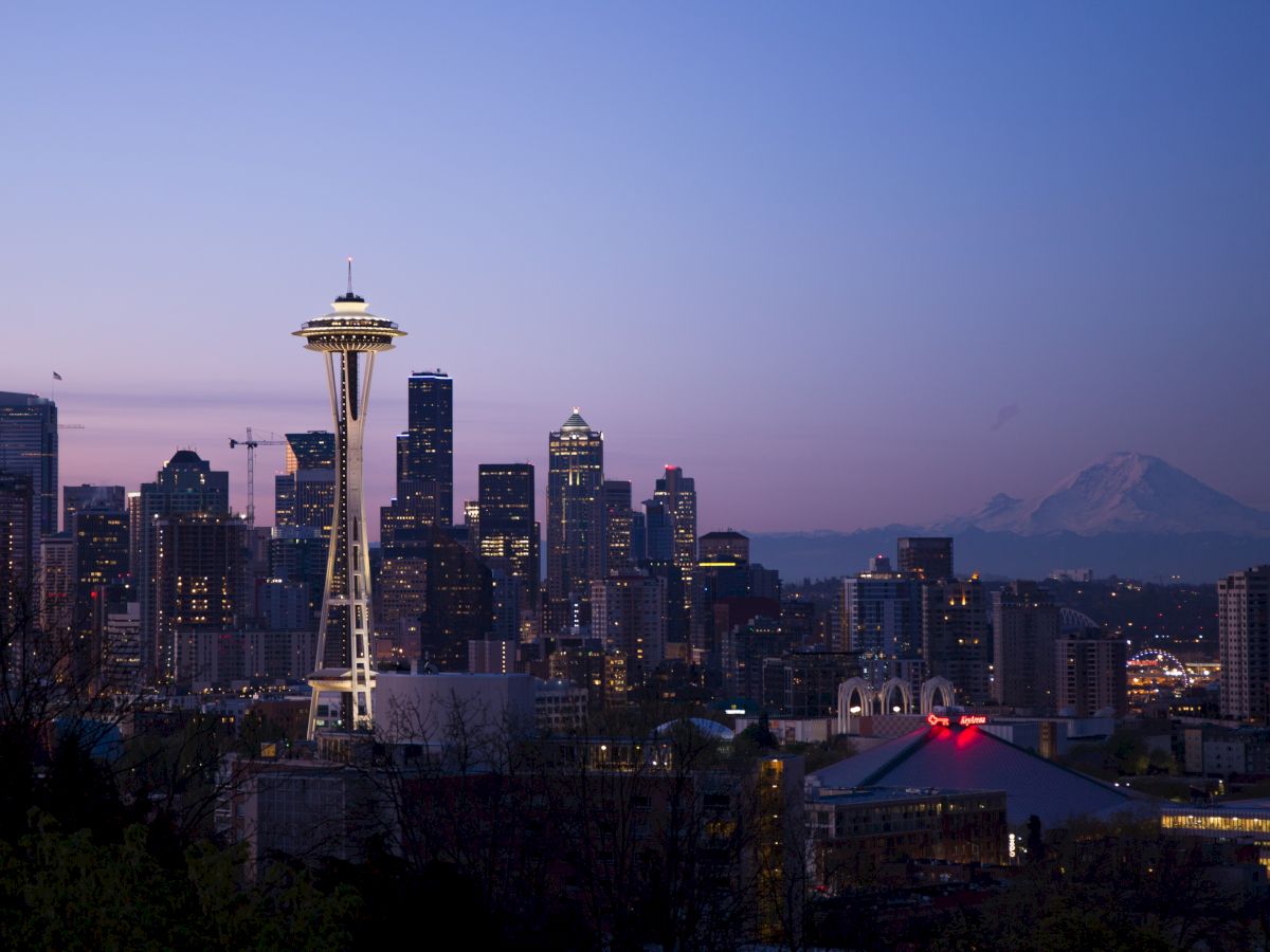 A twilight view of Seattle's skyline featuring the Space Needle, high-rise buildings, and Mount Rainier in the background against a clear evening sky.