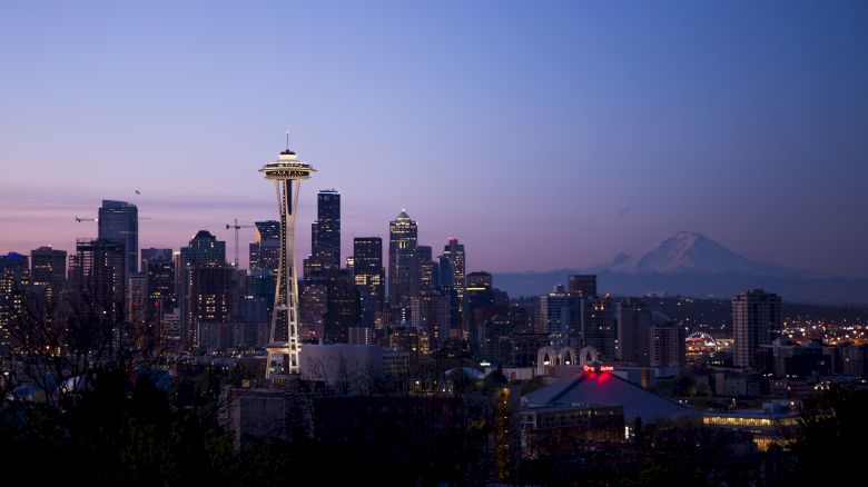 A twilight view of Seattle's skyline featuring the Space Needle, high-rise buildings, and Mount Rainier in the background against a clear evening sky.