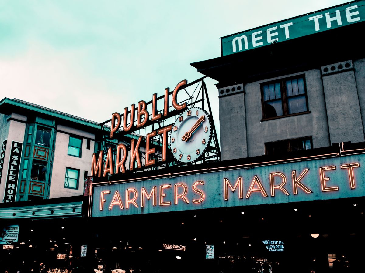 The image shows a neon-lit sign for a "Public Market" and "Farmers Market" in an urban area, likely a well-known market or landmark.