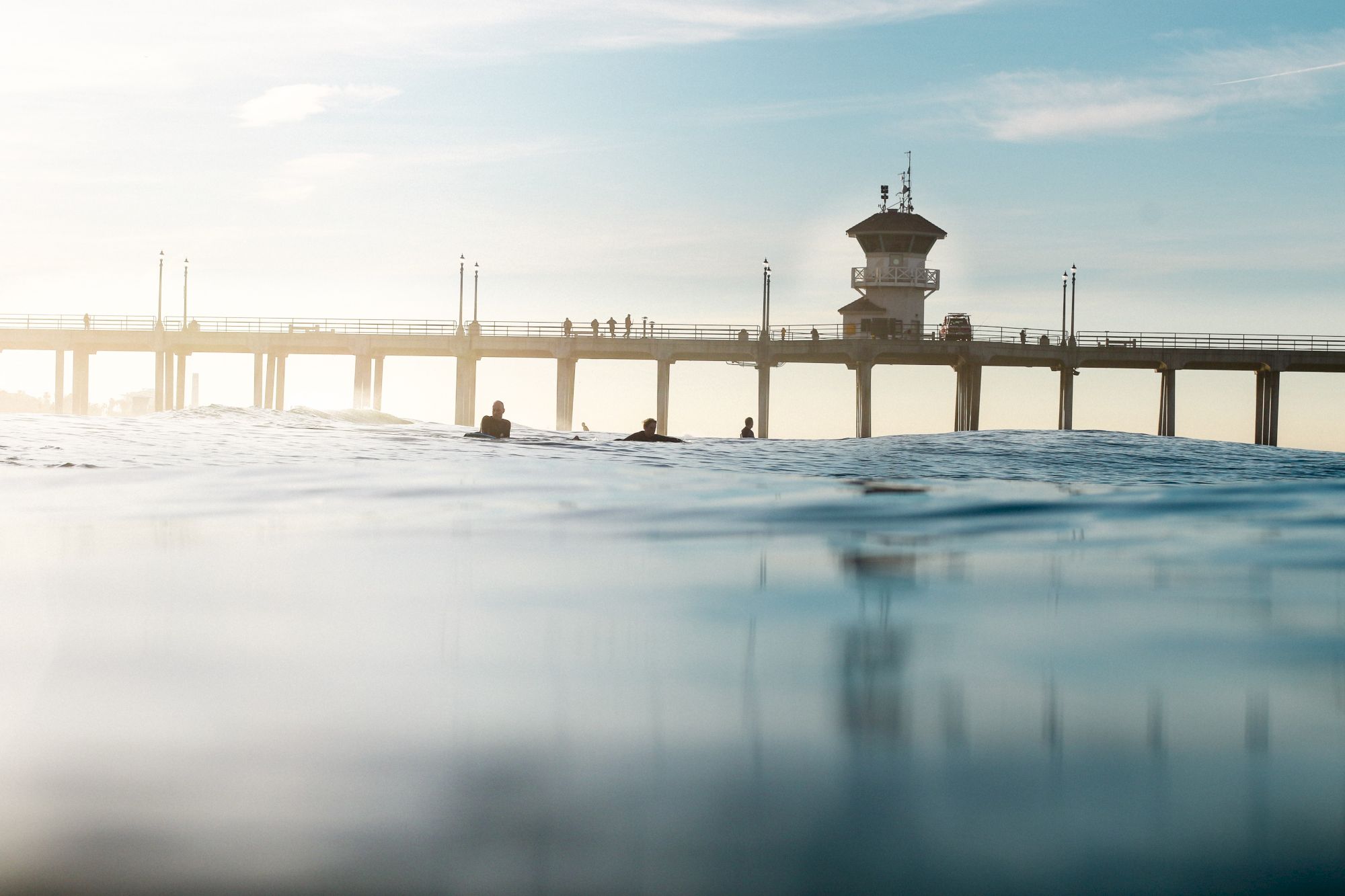 A serene photo of a pier extending into the ocean, with a few people walking on it and a lifeguard tower visible in the background.